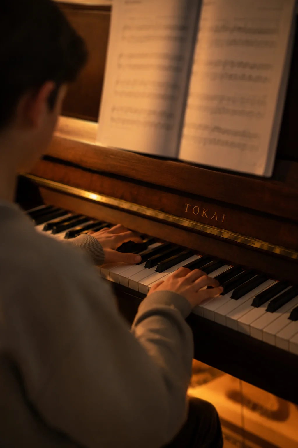 Schüler von hinten beim Klavierspielen mit aufgeschlagenem Notenheft am Tokai-Klavier — Klavierunterricht bei der ARTIQ Musikschule Mainz